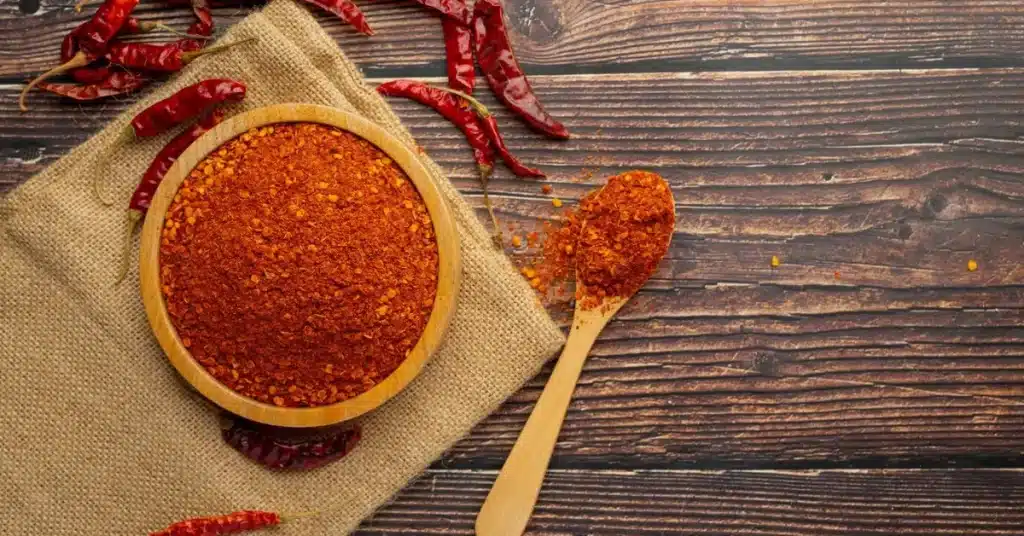 Wooden bowl filled with chili powder, a key ingredient in Cajun seasoning.