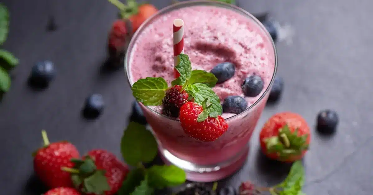 A frozen fruit smoothie in a glass, garnished with fresh berries and mint.