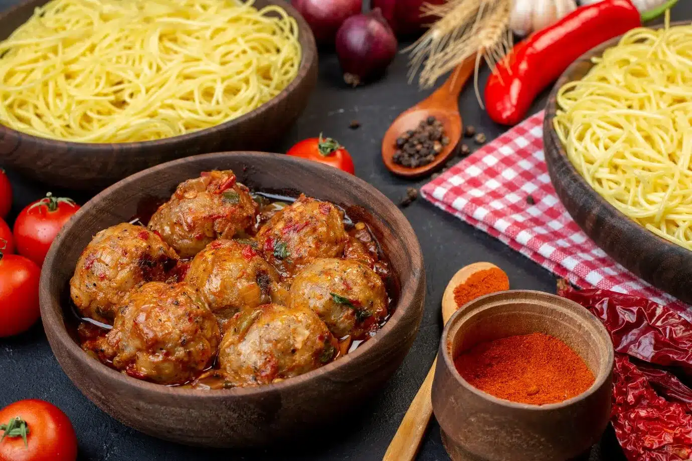 meatball soup in bowl spaghetti in bowl wooden spoons red tomatoes on table